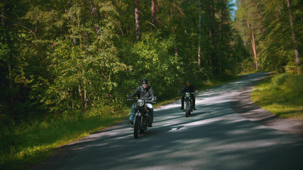 Two bikers are riding fast on the road in the forest