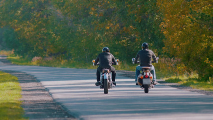 Bikers are riding on the road in the forest near each other