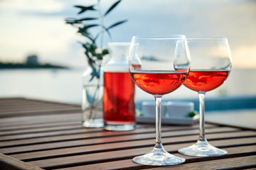 two glasses of rose wine with  olives against blue water on a pier..