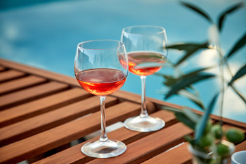 two glasses of rose wine with  olives against blue water on a pier..