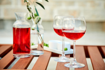 two glasses of rose wine with  olives against blue water on a pier..