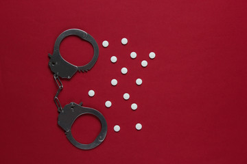 The concept of corruption in medicine. Pills and handcuffs on red background. Medical still life....