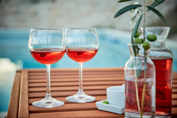 two glasses of rose wine with  olives against blue water on a pier..