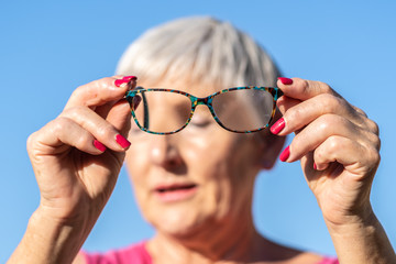 older White haired woman with visión problems and glasses in her hands, blue background