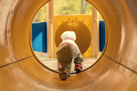  little girl crawling through the tunnel in the playground autumn  day