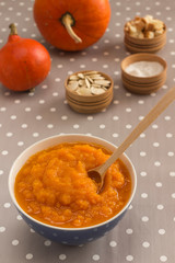 Pumpkin porridge in a blue bowl, orange pumpkins and seeds on a gray polka dot tablecloth