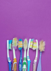 Old used toothbrushes on purple background. Dental care concept. Top view