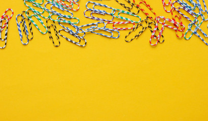 Lot of colored paper clips on yellow background. Minimalistic office concept. Copy space