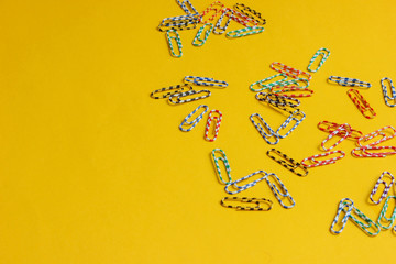 Lot of colored paper clips on yellow background. Minimalistic office concept.