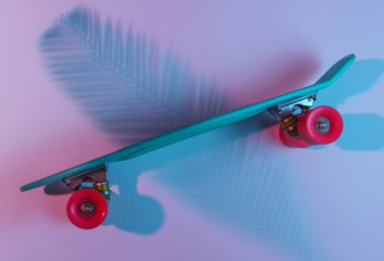 Plastic mini cruiser board on background with shadow from palm leaves. Neon gradient ligh. Top view