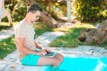 Young man with laptop in outdoor swimming pool.