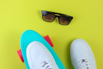 White sneakers on plastic mini cruiser board and sunglasses. Green background. Summertime fun. Top view
