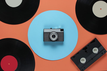 Retro vinyl record video cassette, film camera on a coral color background with a blue circle. Top view