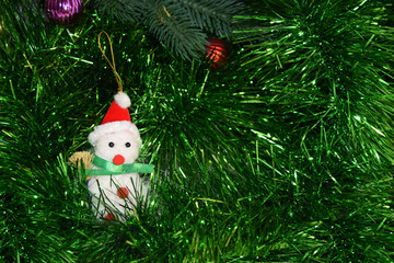 A small toy snowman sits among tinsel under a Christmas tree. Christmas tree toy snowman.