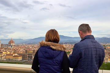 Tourists man and woman look at panorama of historical center of Florence in Italy from Piazzale Michelangelo. Back view