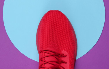 Red sport sneaker on purple background with blue pastel circle. Youth hipster concept. Top view