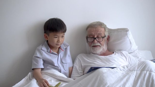 Happy Elderly Senior Man Grandfather Telling Story About Play To Boy Grandson On Bed At Nursing Home