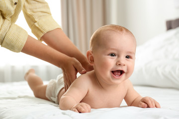 Young woman massaging cute little baby on bed indoors