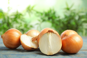 Ripe onions on blue wooden table against blurred background, space for text