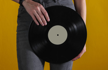 Woman in jeans with vinyl record on yellow background. Crop photo