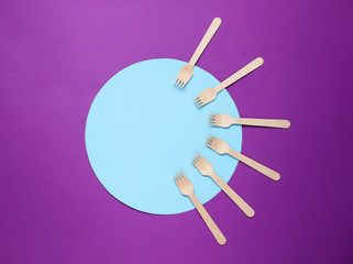 Eco friendly wooden forks on purple background with blue circle. Top view, minimalism