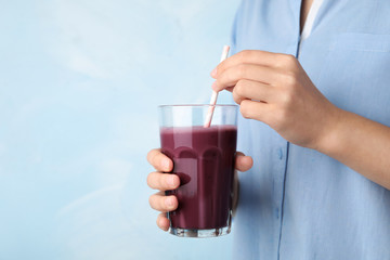 Woman with glass of fresh acai drink and straw on light blue background, closeup. Space for text