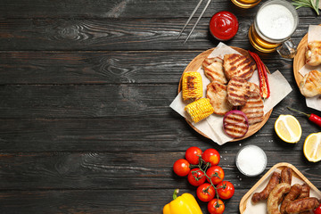 Flat lay composition with barbecued meat and vegetables on black wooden table. Space for text