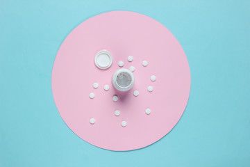 Bottle pills on blue background with pink pastel circle. Top view. Minimalistic medical still life