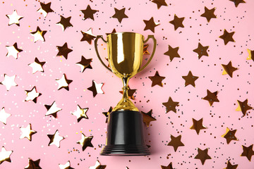 Gold trophy cup and confetti on light pink background, flat lay