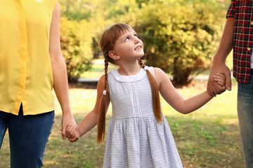 Little girl and her parents holding hands outdoors. Family weekend