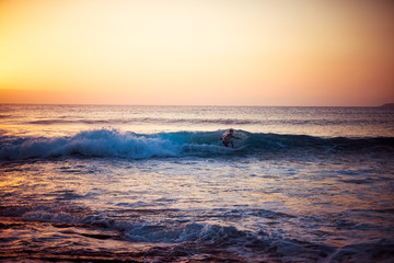 Fototapeta premium The silhouette of a surfer riding a wave at an empty surf spot. Young surfer rides the wave during sunset. Image