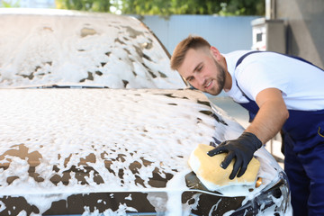 Young worker cleaning automobile with sponge at car wash