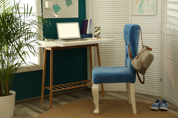 Stylish home workplace with elegant blue chair near window. Interior design