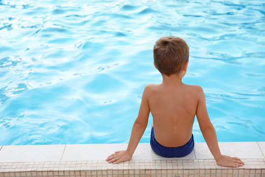 Cute little boy sitting near outdoor swimming pool