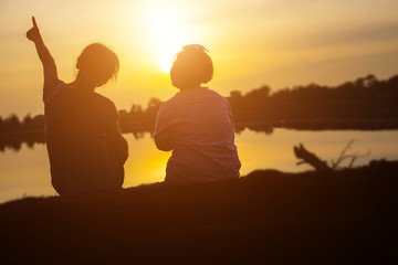 Mother encouraged her son outdoors at sunset, silhouette concept