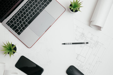 Laptop, phone and rolls of drawings on the Desk in engineering. architectural background with rolls of technical drawings