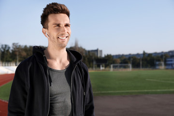 Young sportsman with wireless earphones at stadium