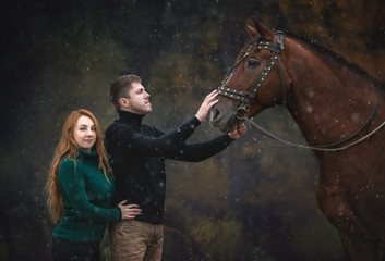 Beautiful young couple with a horse outdoors. Young lady embracing a man. 
