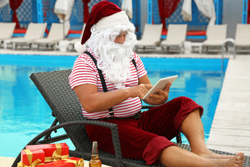 Obraz premium Authentic Santa Claus with tablet resting on lounge chair at resort