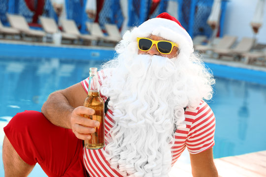 Authentic Santa Claus with bottle of beer near pool at resort