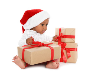 Festively dressed African-American baby with Christmas gifts on white background