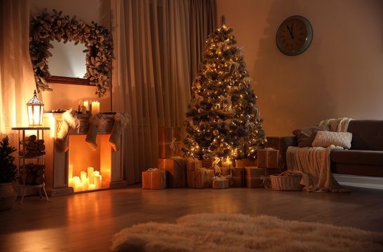 Stylish interior with decorative fireplace and beautiful Christmas tree in evening