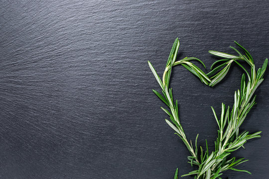 Heart shaped aromatic rosemary plant on black stone background. Template Italian restaurant menu. Template food blog social media. Fresh organic food concept. Copy space for your design.