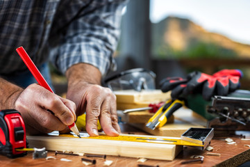 Adult carpenter craftsman with a pencil and the carpenter's square trace the cutting line on a wooden table. Construction industry, housework do it yourself. Stock photography.