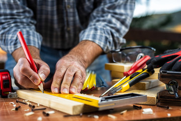 Adult carpenter craftsman with a pencil and the carpenter's square trace the cutting line on a wooden table. Construction industry, housework do it yourself. Stock photography.