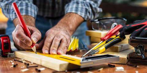 Adult carpenter craftsman with a pencil and the carpenter's square trace the cutting line on a wooden table. Construction industry, housework do it yourself. Stock photography.