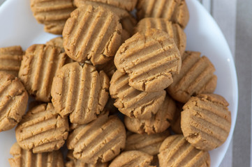 Pile of peanut butter biscuits on white plate, very tasty golden baked sweets, cookies served to eat