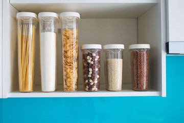Stocked kitchen pantry with food - pasta, buckwheat, rice and sugar , side view. The organization and storage in kitchen of a case with grain in plastic containers.
