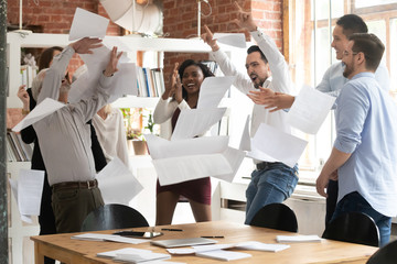 Overjoyed diverse employees throw papers celebrating success