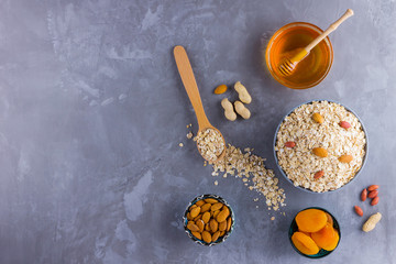 Ingredients for a healthy breakfast, nuts, oatmeal, honey, dried apricots, almonds, peanuts. Concept of natural organic food in season. Flat lay